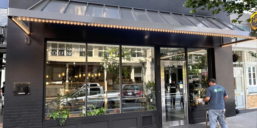 Modern storefront with metal canopy, potted plants, and LED lighting